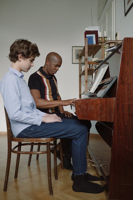 A teacher instructs a student during a piano lesson indoors, both focused on playing.