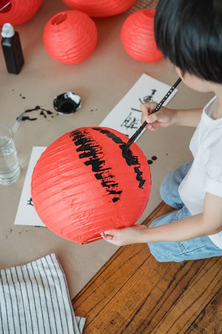 A child artistically painting a red lantern using calligraphy brush indoors.